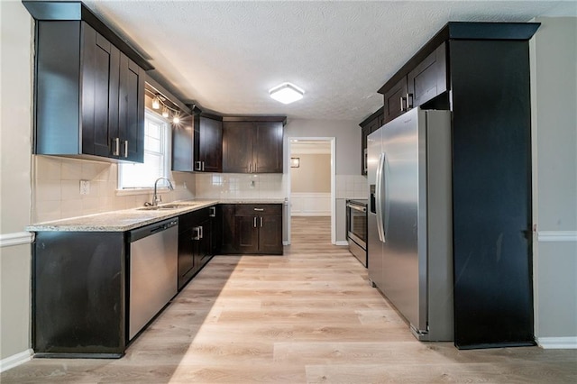 kitchen with appliances with stainless steel finishes, a sink, light wood-style floors, light countertops, and a textured ceiling