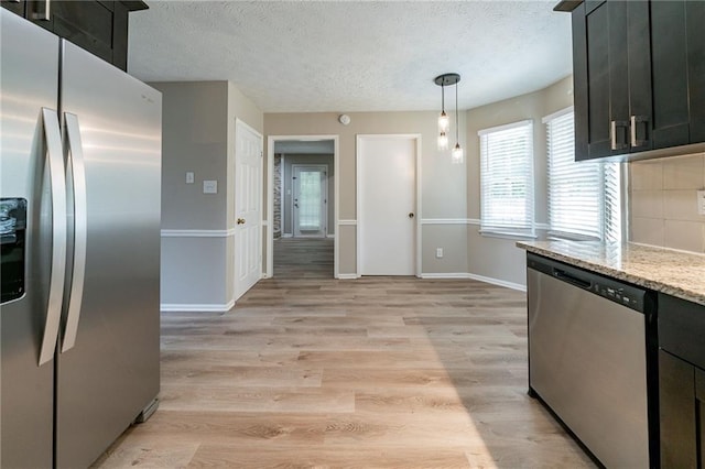kitchen featuring decorative backsplash, a textured ceiling, appliances with stainless steel finishes, baseboards, and light wood finished floors