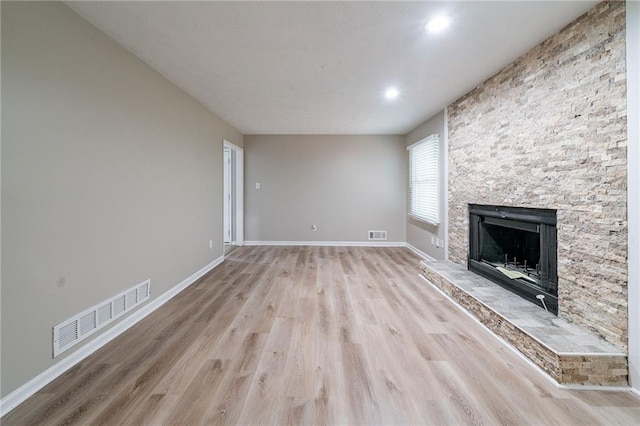 unfurnished living room featuring baseboards, visible vents, a stone fireplace, and light wood-style flooring
