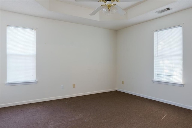 empty room featuring baseboards, visible vents, a ceiling fan, a raised ceiling, and dark carpet