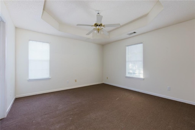 spare room with baseboards, a raised ceiling, visible vents, and a healthy amount of sunlight