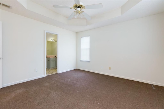 unfurnished room with a tray ceiling, visible vents, dark carpet, ceiling fan, and baseboards