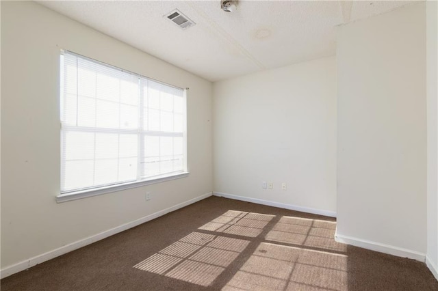 unfurnished room with visible vents, dark carpet, and baseboards