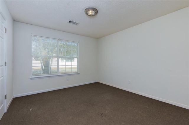 spare room with baseboards, visible vents, dark colored carpet, and a textured ceiling