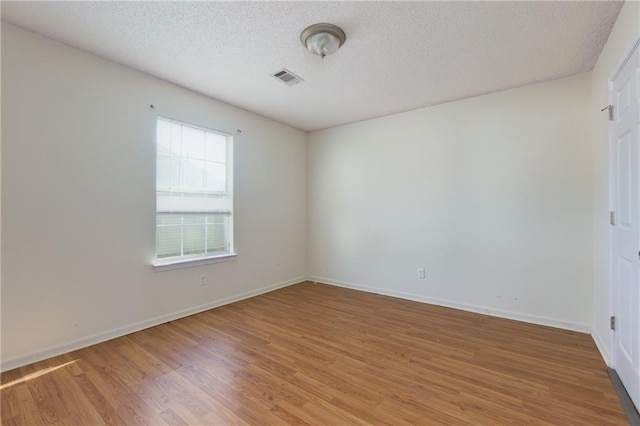 unfurnished room with baseboards, a textured ceiling, visible vents, and wood finished floors