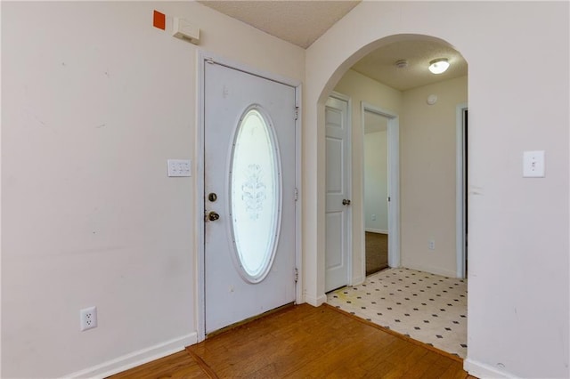 foyer featuring arched walkways, wood finished floors, and baseboards