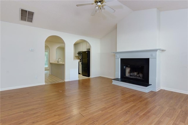 unfurnished living room featuring light wood-type flooring, visible vents, a fireplace with raised hearth, and lofted ceiling