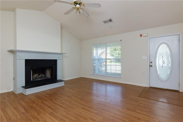 entryway with visible vents, a fireplace with raised hearth, a ceiling fan, light wood-style flooring, and vaulted ceiling