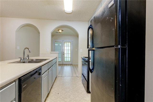 kitchen featuring light floors, light countertops, a textured ceiling, black appliances, and a sink