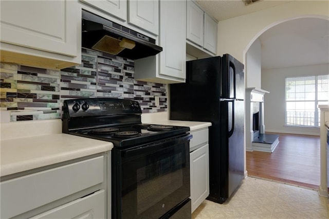 kitchen featuring black / electric stove, under cabinet range hood, white cabinets, light countertops, and decorative backsplash