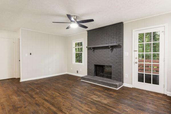 unfurnished living room featuring dark wood-type flooring, ornamental molding, a fireplace, and ceiling fan