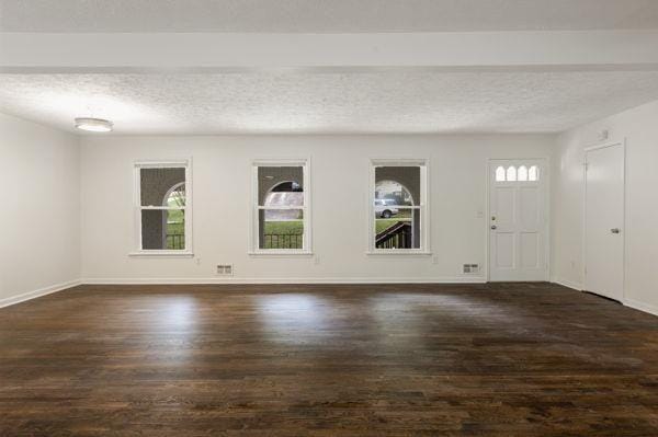 interior space with dark wood-type flooring, a wealth of natural light, and beamed ceiling