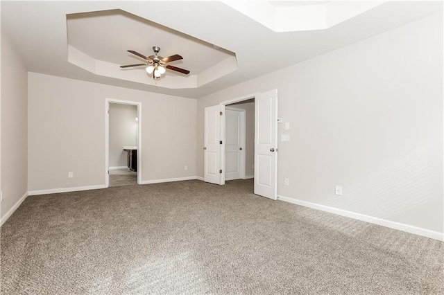 unfurnished bedroom with ceiling fan, a raised ceiling, carpet floors, and ensuite bath