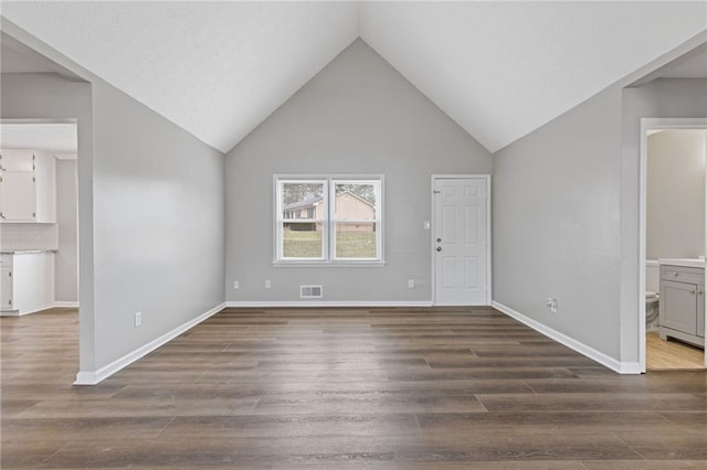 unfurnished living room featuring high vaulted ceiling and dark hardwood / wood-style flooring