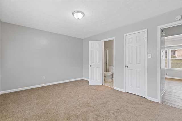 unfurnished bedroom featuring ensuite bathroom, light carpet, and a textured ceiling