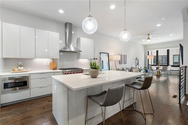 kitchen with dark wood-type flooring, wall chimney range hood, a breakfast bar area, and modern cabinets