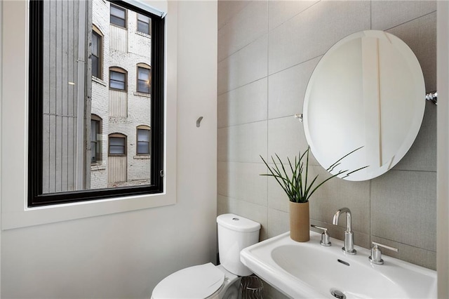 bathroom featuring a sink, tile walls, and toilet