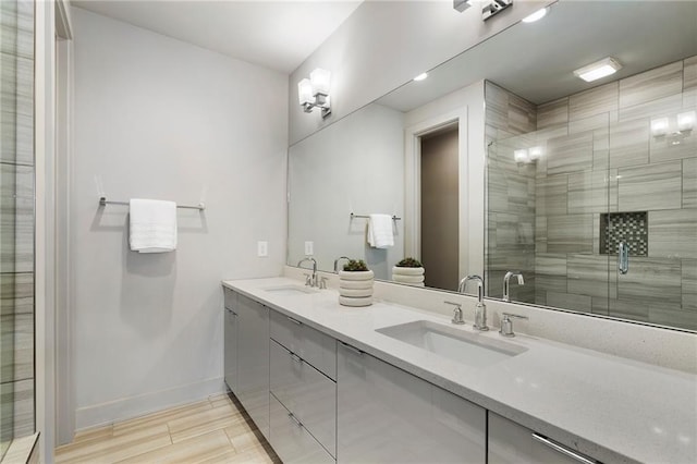 full bathroom with double vanity, a stall shower, a sink, and baseboards