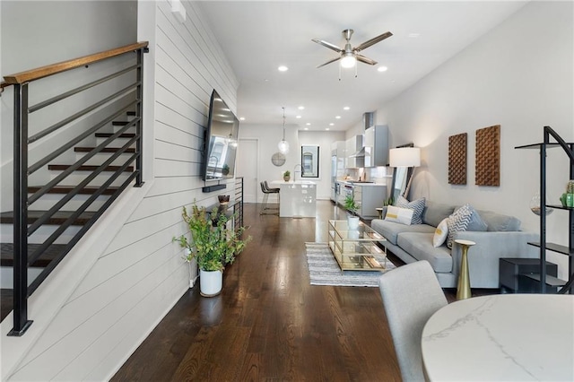 living room with recessed lighting, ceiling fan, wooden walls, wood finished floors, and stairs