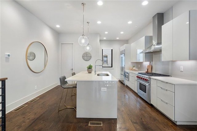 kitchen with a breakfast bar area, high end appliances, a sink, modern cabinets, and wall chimney exhaust hood