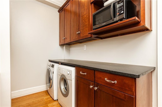 clothes washing area featuring light wood finished floors, baseboards, cabinet space, and washing machine and clothes dryer