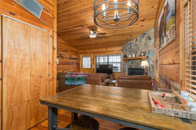 dining area featuring vaulted ceiling, ceiling fan with notable chandelier, a fireplace, wooden ceiling, and wood walls