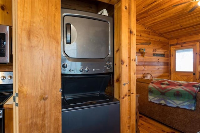 laundry room featuring wood finished floors, wooden ceiling, wood walls, stacked washer and dryer, and laundry area