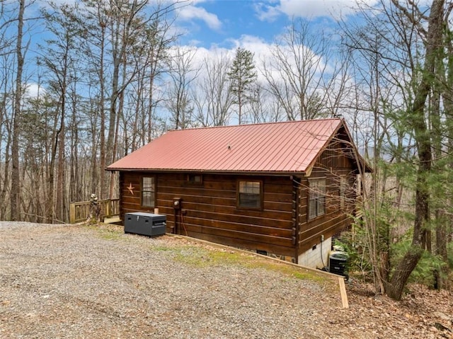 view of side of home with gravel driveway, log siding, central air condition unit, and metal roof