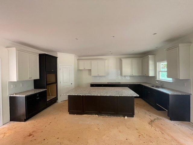 3292 Mill Forest Dr, Conyers, GA 30094 - kitchen featuring a kitchen island, backsplash, white cabinetry, a sink, and light stone countertops