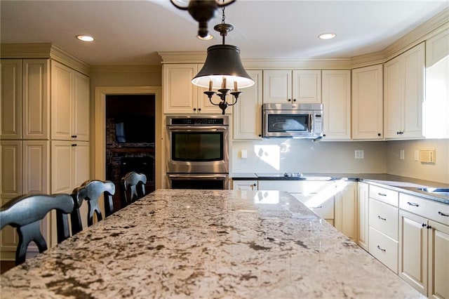 kitchen with hanging light fixtures, stainless steel appliances, cream cabinets, a kitchen bar, and ornamental molding