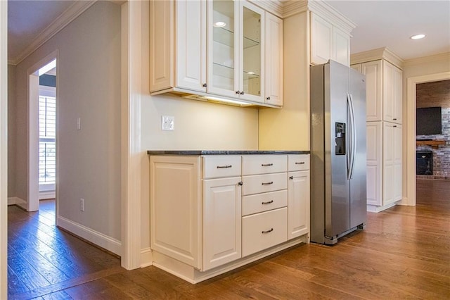 kitchen with white cabinetry, a brick fireplace, stainless steel fridge with ice dispenser, dark hardwood / wood-style flooring, and ornamental molding