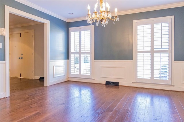 empty room with ornamental molding, dark wood-type flooring, a healthy amount of sunlight, and an inviting chandelier