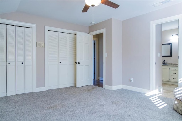 unfurnished bedroom with ensuite bath, ceiling fan, light carpet, and two closets