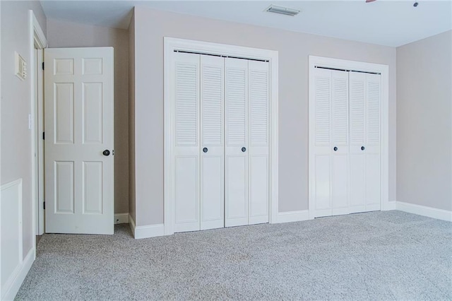 unfurnished bedroom featuring two closets and light colored carpet