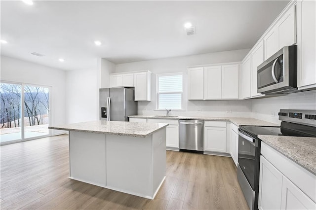 kitchen with white cabinetry, stainless steel appliances, a center island, and light stone counters