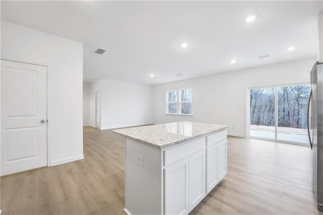 kitchen with light stone counters, light hardwood / wood-style flooring, a center island, and white cabinets