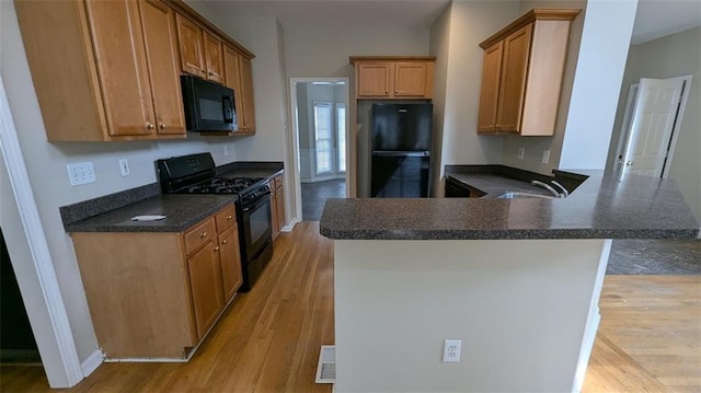 kitchen featuring dark countertops, light wood-style flooring, a peninsula, black appliances, and a sink