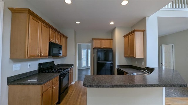 kitchen featuring light wood-type flooring, dark countertops, black appliances, and a peninsula