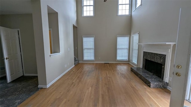 unfurnished living room featuring a towering ceiling, wood finished floors, baseboards, and a high end fireplace