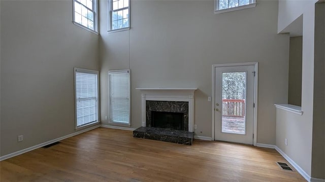 unfurnished living room with wood finished floors, visible vents, a high end fireplace, and baseboards