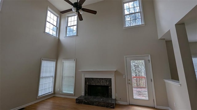 unfurnished living room featuring wood finished floors, a towering ceiling, a high end fireplace, baseboards, and ceiling fan