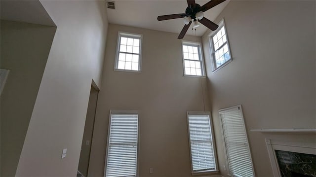 unfurnished living room featuring visible vents, a ceiling fan, a high ceiling, and a fireplace