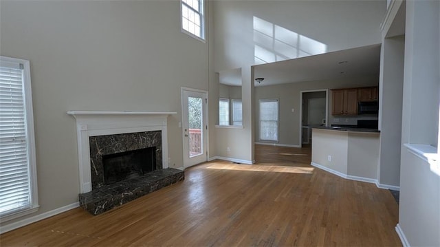 unfurnished living room featuring wood finished floors, a fireplace, baseboards, and a towering ceiling