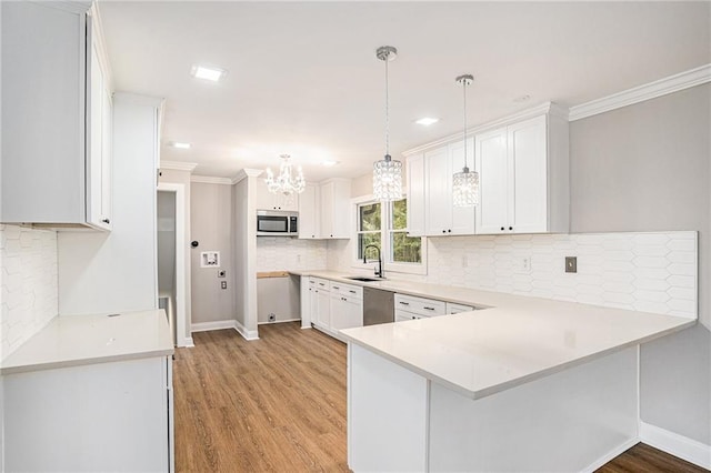 kitchen featuring appliances with stainless steel finishes, a peninsula, light countertops, light wood-type flooring, and a sink