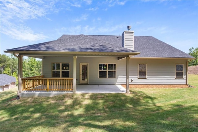 back of house with a patio area, a lawn, roof with shingles, and a chimney