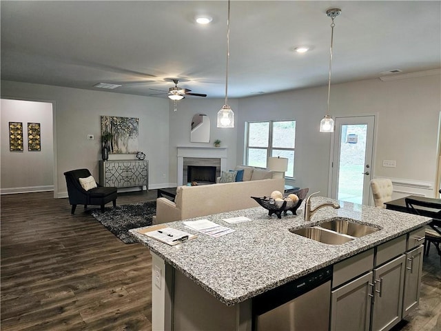 kitchen with a sink, a center island with sink, a fireplace, dark wood-style floors, and stainless steel dishwasher