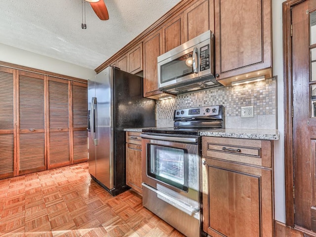 kitchen featuring ceiling fan, a textured ceiling, appliances with stainless steel finishes, tasteful backsplash, and light parquet flooring