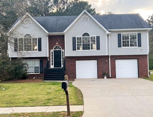 raised ranch with a front yard, a garage, brick siding, and driveway