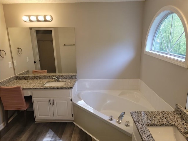 full bath featuring vanity, a garden tub, a walk in closet, and wood finished floors