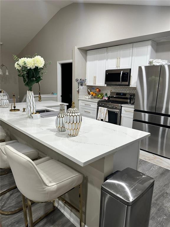 kitchen featuring backsplash, light stone countertops, vaulted ceiling, appliances with stainless steel finishes, and white cabinets